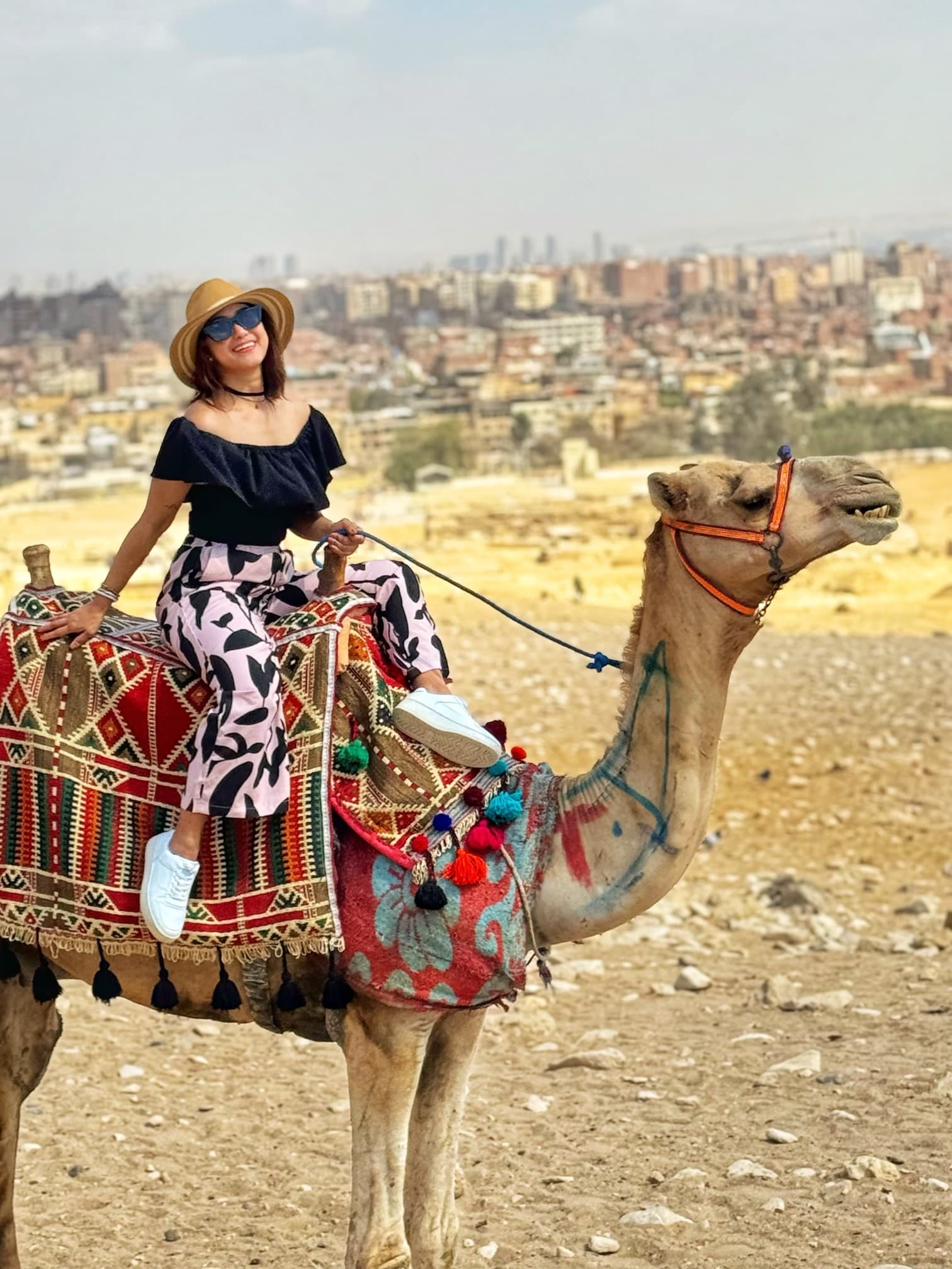 J-Ann riding a camel in front of the Cairo skyline